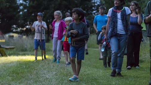 Group of families with children of different ages holding bat detectors in a field at dusk.